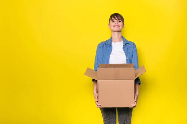 段ボール箱の移動と黄色の背景の上に立ってきれいな女性 — ストック写真