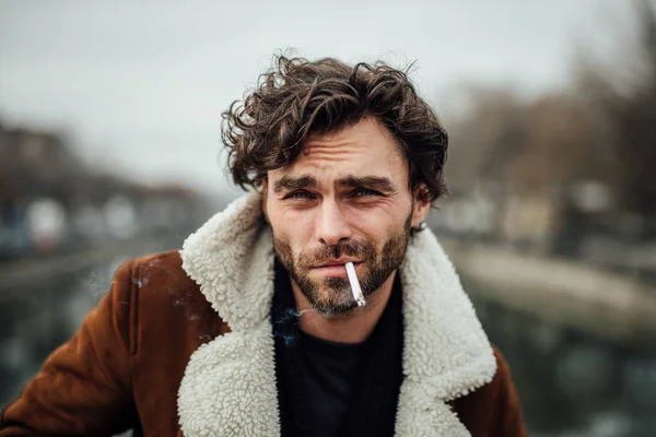凉爽英俊的男子吸烟香烟外面在一个飞行员的外套与男性的态度等待一些 — 图库照片