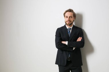 yan emin seyir emin zarif adam katlanmış silah karşı takım elbise ve kravat, beyaz bir duvar ile ayakta