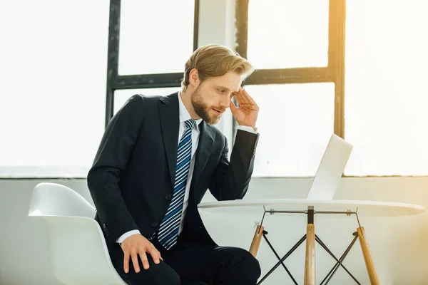 elegant man in suit, tired of office work, worried about something, being in his office looking at his laptop