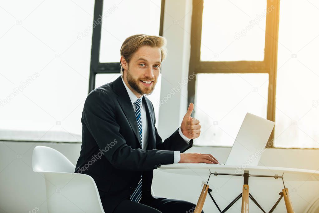 stylish man in costume, sales manager, looking confidently and smile at the camera in his office near the window, showing ok sign