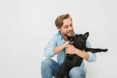 Genç sarışın adam, yakışıklı adam, oynama ve beyaz zemin üzerine köpeği sevmek
