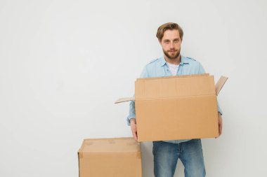bazı karton kutular taşıyan genç bir sarışın adam, teslimatçı veya şeyler için başka bir ev beyaz bir arka plan üzerinde kameraya bakarak hareket eden bir adam