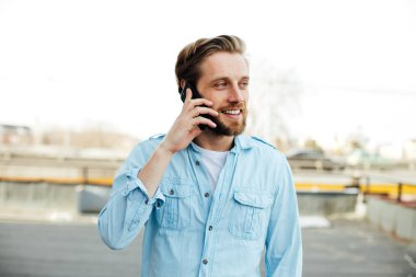 bir yerde dışında gülümseyen ve bu konuşma zevk cep telefonu, konuşurken rahat genç adam mavi gömlekli, muhabbet
