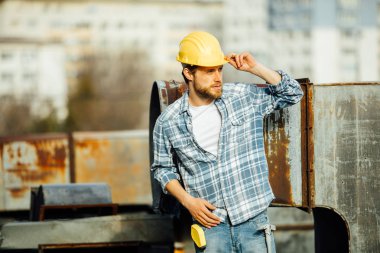 işçisi kask ile araçlar, kafasına ile bir şal gömlekli sakallı güçlü bir adam, bir yerde dışında üzerinde çalışmaya ilgi tarafa bakarak paslı bir şantiye başlamak için hazır