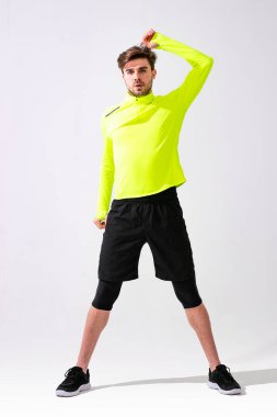 Önce esneme hareketleri yap. Spor giyim eğitimi alan genç bir adam beyaz arka planda kaslarını esnetiyor.