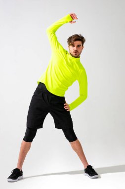 Önce esneme hareketleri yap. Spor giyim eğitimi alan genç bir adam beyaz arka planda kaslarını esnetiyor.