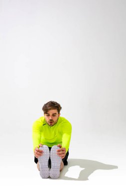 Önce esneme hareketleri yap. Spor giyim eğitimi alan genç bir adam beyaz arka planda kaslarını esnetiyor.