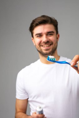 Diş fırçasını diş macunuyla kameraya gösteren genç bir adamı çek.