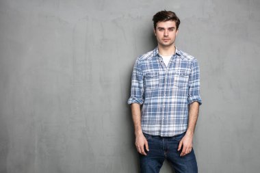 Gri arka plan beton duvarda duran normal bir genç adam.