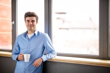 Evde kal. Resmi kıyafetli genç bir adam pencerenin yanında dikiliyor.