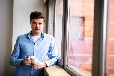 Kendi evinde, pencerenin yanında duran izole bir adam.