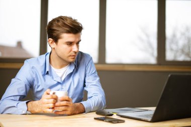 Yakışıklı bir adam, girişimci. Ofis masasında laptopuyla kahve içiyor.