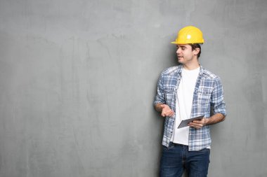 Endüstriyel beton duvarın üzerinde duran ve bitirmesi gereken proje için tablet üzerinde çalışan genç bir mühendis.