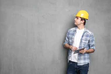 Harekete geçmeden önce düşünün, güvenlik kaskı ve modern tabletli genç işçiler sahip olduğu projeyi bitirmek için bir çözüm arıyorlar, beton duvarın üzerinde duruyorlar.