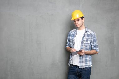 Endüstriyel beton duvarın üzerinde duran ve bitirmesi gereken proje için tablet üzerinde çalışan genç bir mühendis.