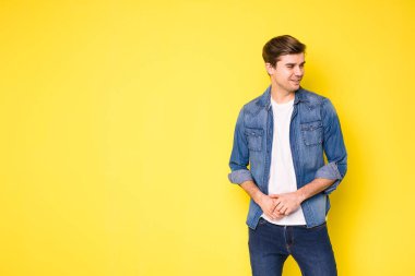 Sarı arka planda kot pantolon giyen basit ve havalı bir adam.