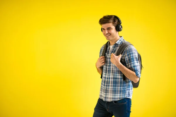 黄色の背景で学校に行く途中で音楽を聞いている現代的でクールな若い学生 — ストック写真