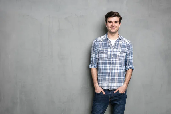 Gülümseyen gevşek adam gri beton bir duvarda duruyor, kameraya neşeli görünüyor.