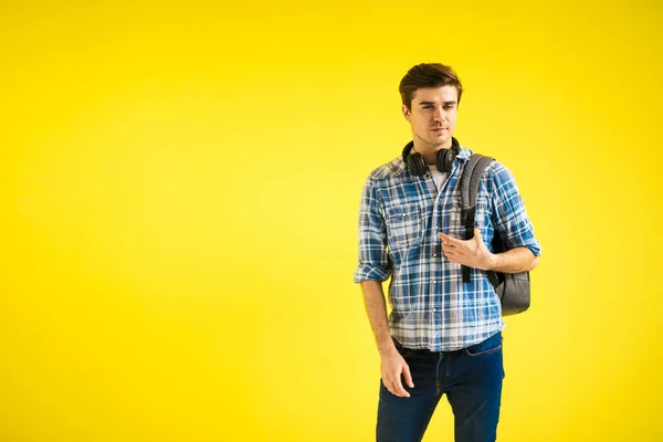 仕事のための服は何ですか 黄色の背景にバックパックとヘッドフォンを持つ若い人は — ストック写真