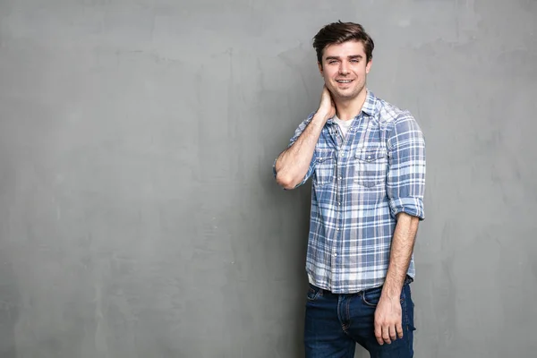 smiling relaxed man standing on a grey concrete wall, looking joyful to the camera