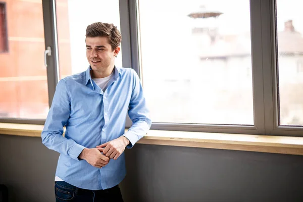 Thoughtful entrepreneur standing next to a window, having break, deep in thoughts, enjoying view, waiting for meeting to start, making business decision