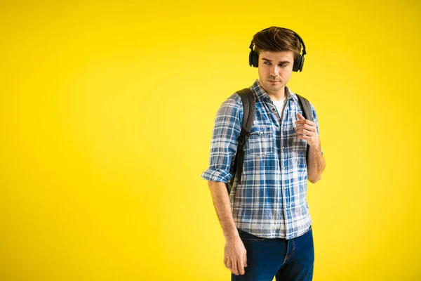 黄色の背景で学校に行く途中で音楽を聞いている現代的でクールな若い学生 — ストック写真