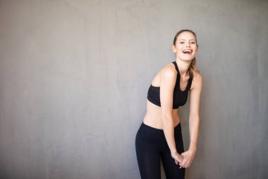 Spor giyimde aktif ve sportif bir kadın kameraya olumlu bakıyor ve gülümsüyor.