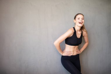 Spor giyimde aktif ve sportif bir kadın kameraya olumlu bakıyor ve gülümsüyor.