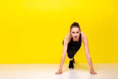 Sarı arka planda siluetli bir kadın koşucu. Çekici bir kadının şık spor elbiseli fotoğrafı. Dinamik hareket. Yan görüş. Spor ve sağlıklı yaşam tarzı