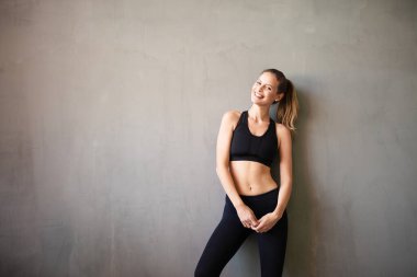 Spor giyimde aktif ve sportif bir kadın kameraya olumlu bakıyor ve gülümsüyor.