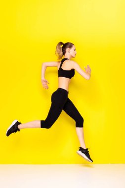 Sarı arka planda siluetli bir kadın koşucu. Çekici bir kadının şık spor elbiseli fotoğrafı. Dinamik hareket. Yan görüş. Spor ve sağlıklı yaşam tarzı