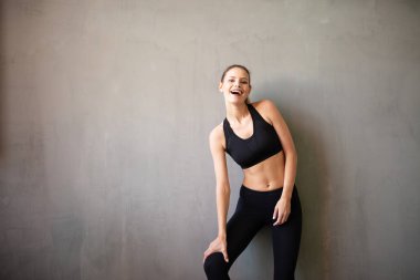 Spor giyimde aktif ve sportif bir kadın kameraya olumlu bakıyor ve gülümsüyor.