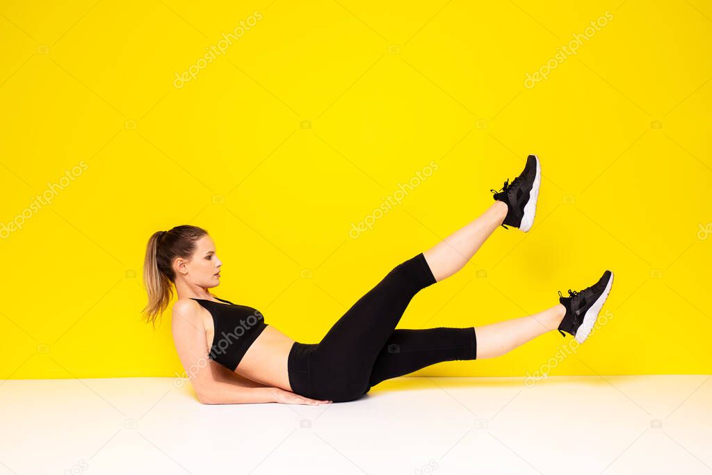 athletic woman in sportwear execise her abs, doing some sport exercise on the floor for the hips and abs, on yellow background