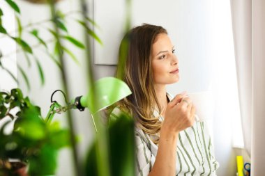 Kendinle mutlu ol. Bekar bir kadın evde takılıyor, kitap okuyor, açık bir pencerenin yanında kahve içiyor.