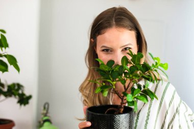 Evinize iyi bakın ve sevin bitkiler, kollarında bir bonsai tutan genç kadın neşe ve sevgiyle, ev sağlığı aktivitesi