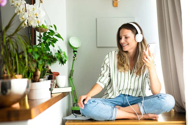 happy single woman comunicating and listening music on the desk next to the plants and bright window, work from home, stay at home.