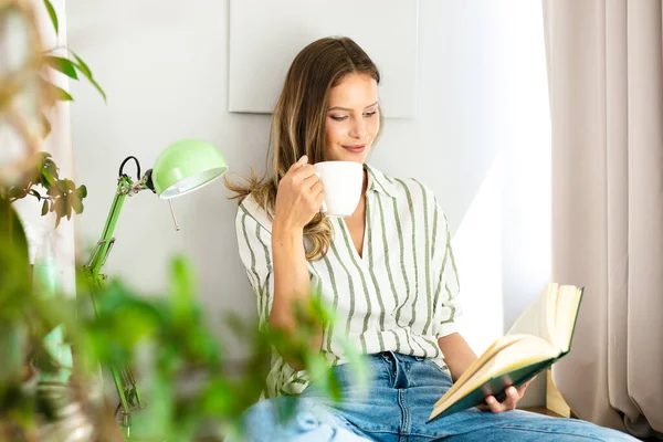 Kadın Parlak Bir Pencerenin Yanında Kitap Okuyor Dinleniyor Kahve Içiyor - Stok İmaj