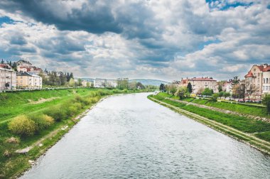 Şiddetli yağmur bulutlarının altında sınırda yeşil çimenler olan dar bir nehir.