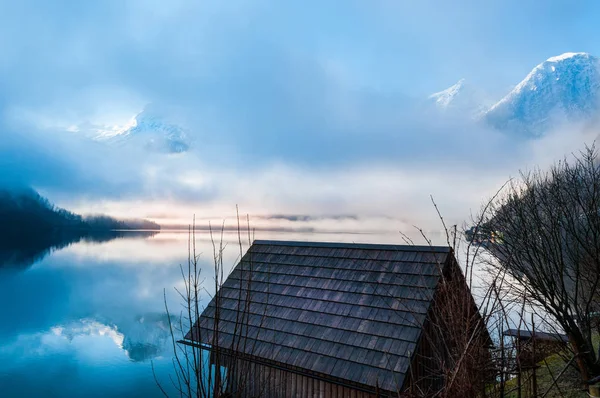 Kleines Holzhaus am Ufer des Sees mit nebligem Berg — Stockfoto