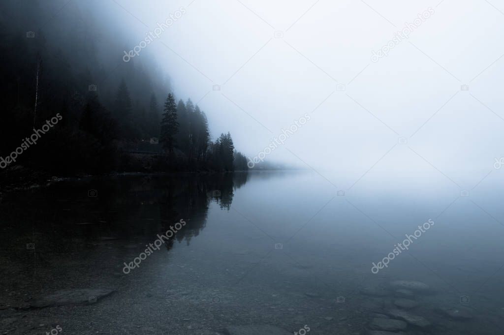 Foggy morning on the border of calm lake in Austrian Alps