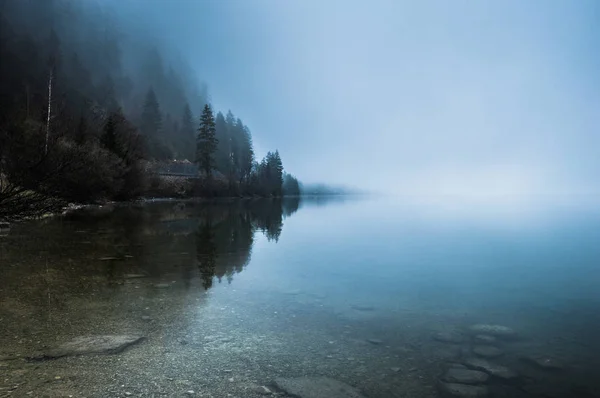 Mattinata nebbiosa al confine del lago calmo nelle Alpi austriache Fotografia Stock