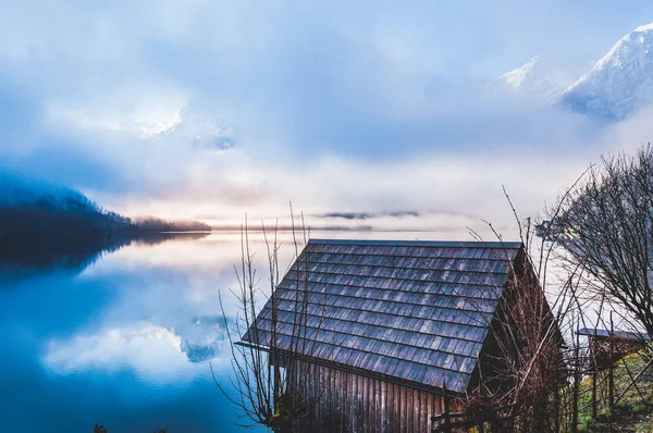 Kleines Holzhaus am Ufer des Sees mit nebligem Berg — Stockfoto