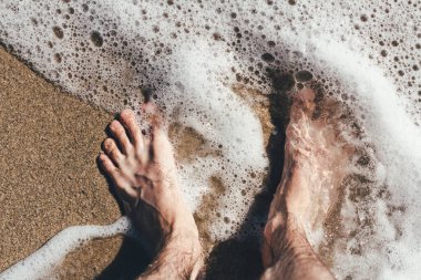 Deniz dalgalarındaki bacaklar kumlu sahile bakan deniz dalgaları