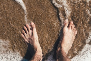 Deniz dalgalarındaki bacaklar kumlu sahile bakan deniz dalgaları