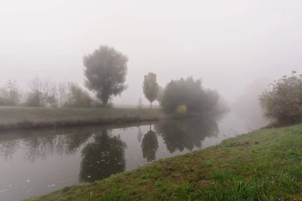 Foggy autunno o inverno mattina su un fiume, passeggiata con panchina — Foto Stock