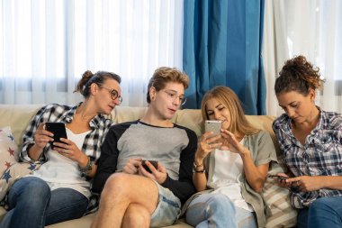 Gayri resmi olarak giyinmiş bir grup genç, yemek odasındaki bir kanepede oturup cep telefonuna bakıyor. Yaşam biçimi