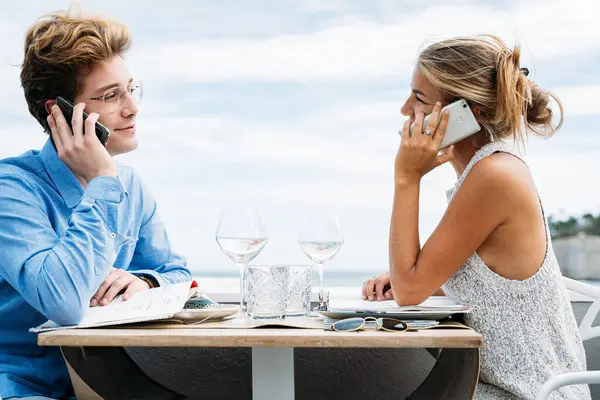 Młoda Para Rozmawia Przez Telefon Siedząc Przy Stole Restauracji — Zdjęcie stockowe