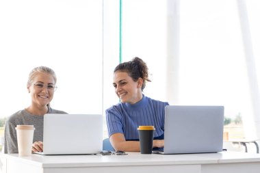 İki kız gülümsüyor ve bir ofiste dizüstü bilgisayarla çalışıyorlar.