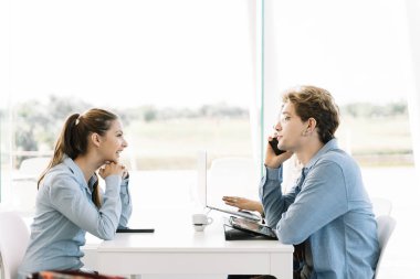 Bir grup genç, iş arkadaşının masasında pencerenin yanındaki dizüstü bilgisayarlarla bir masada oturuyor.